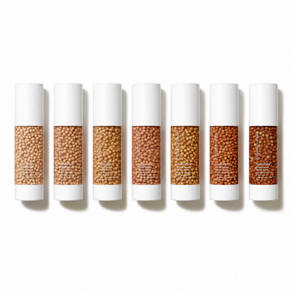 Six white cosmetic tubes arranged in a row on a white background, each showing a different shade of tan and brown seed beads in the clear center window.