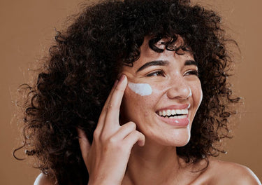 Happy, smiling lady applying moisturiser to her face