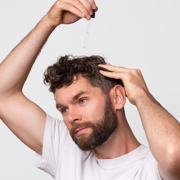 Man applying a dropper of liquid to his hair against a white background