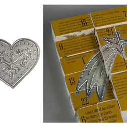 Silver-toned metal bookmarks shaped like a heart and a star, displayed alongside yellow booklets with printed text and numbers.