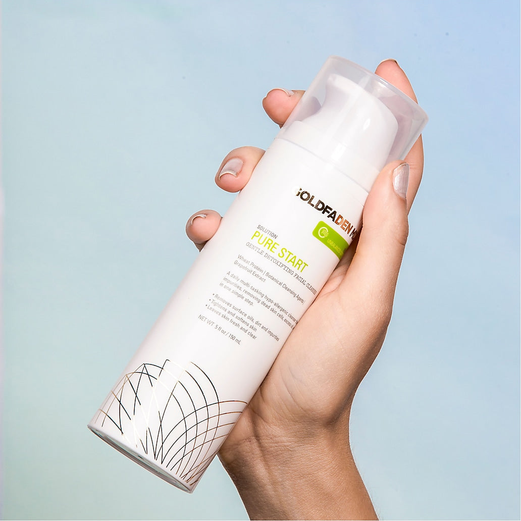 Hand holding a skincare product with visible brand name against a light blue background