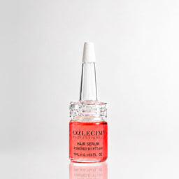 A bottle of Colcemini Professional Hair Serum with a white applicator cap, filled with a vibrant pinkish-red liquid, set against a clean white background with a soft reflection.