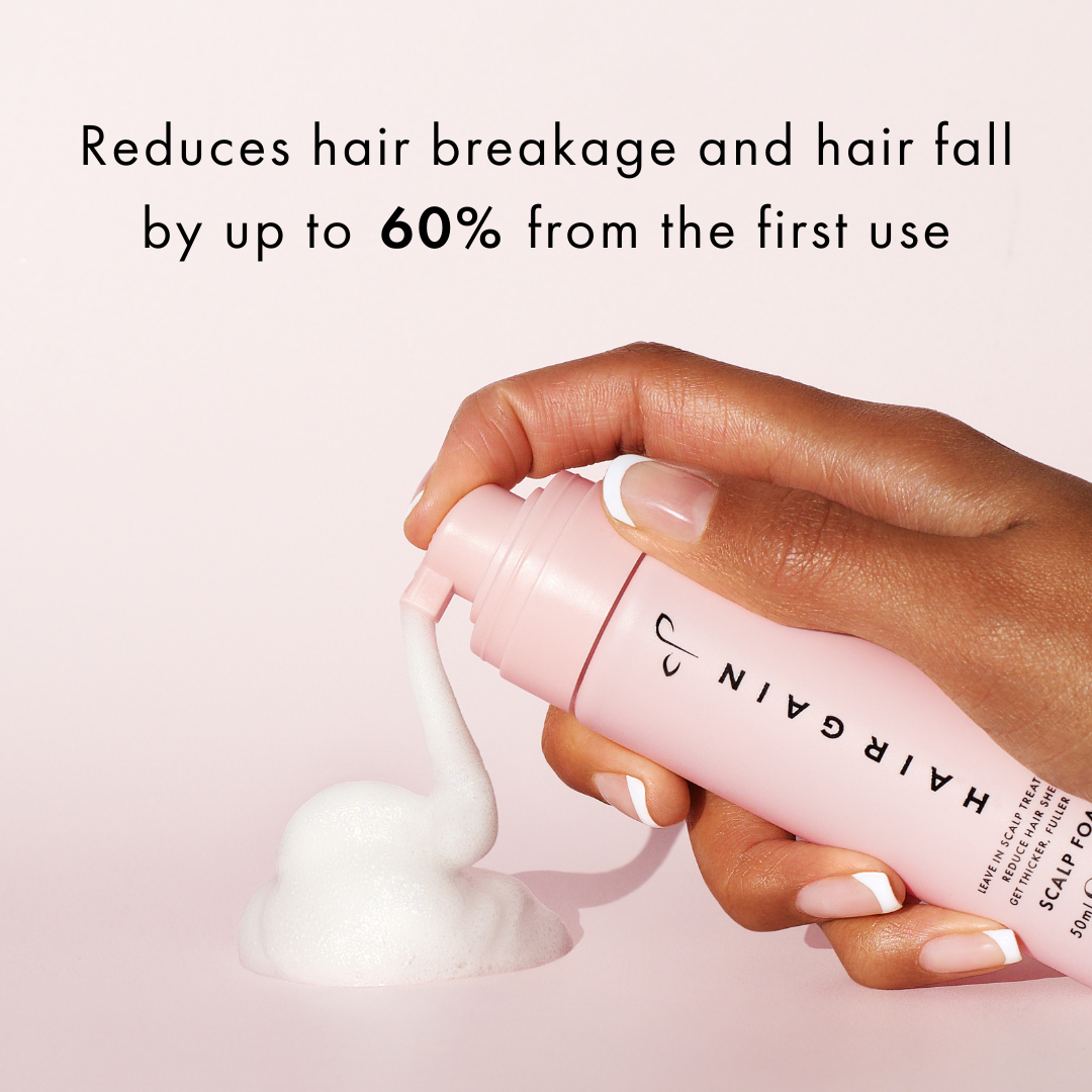 Hand holding a pink bottle of Hairgain scalp tonic with text on a light pink background
