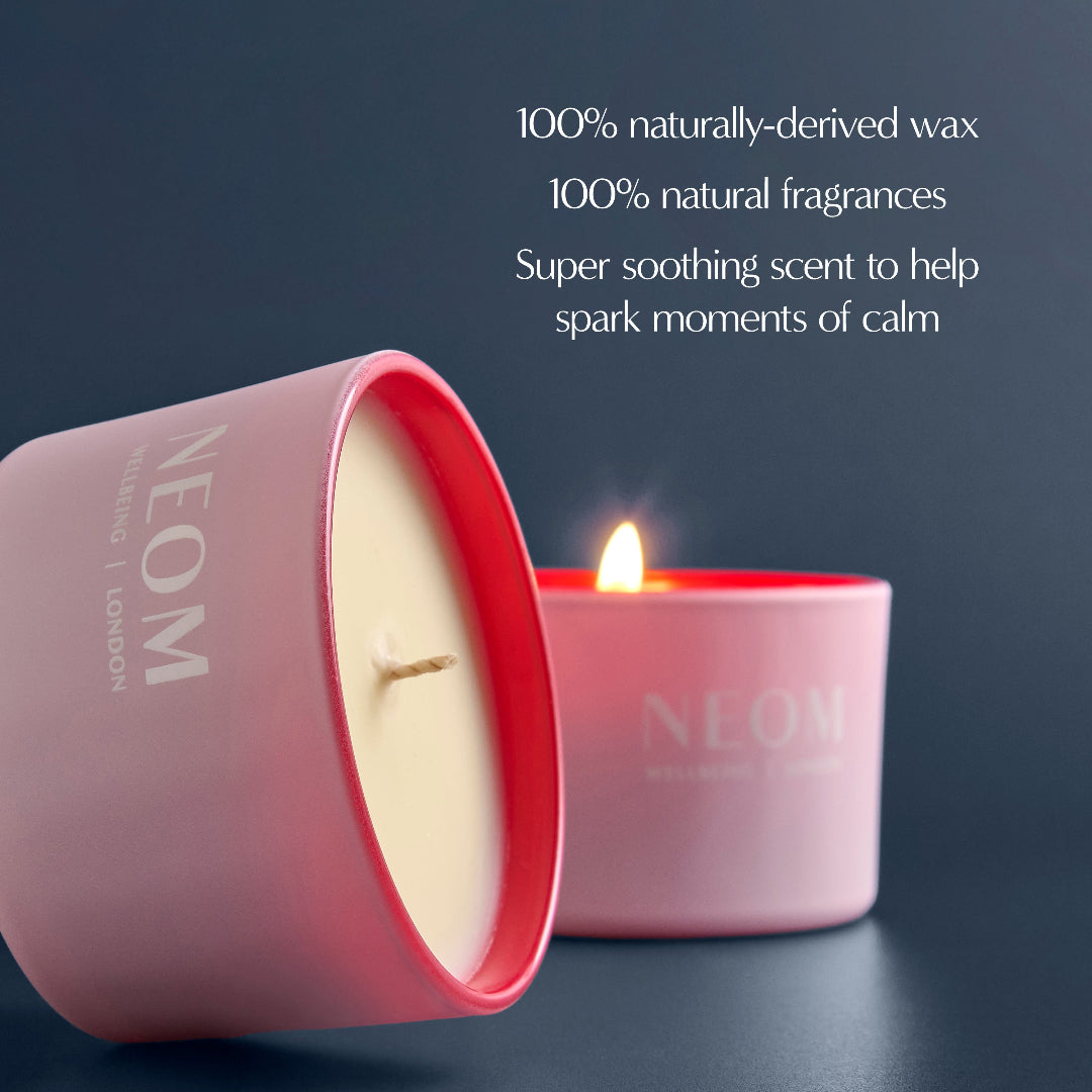 NEOM candle with a lit wick on a dark background