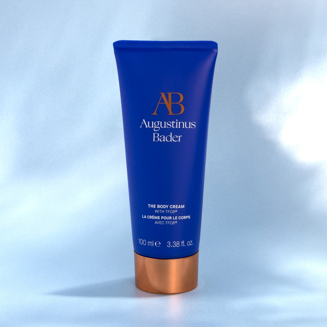 Blue tube of Augustinus Bader body cream on a light blue background