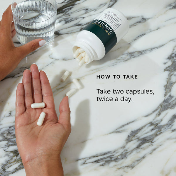 Hand holding two capsules with a bottle and glass of water on a marble surface, featuring text on how to take the capsules.