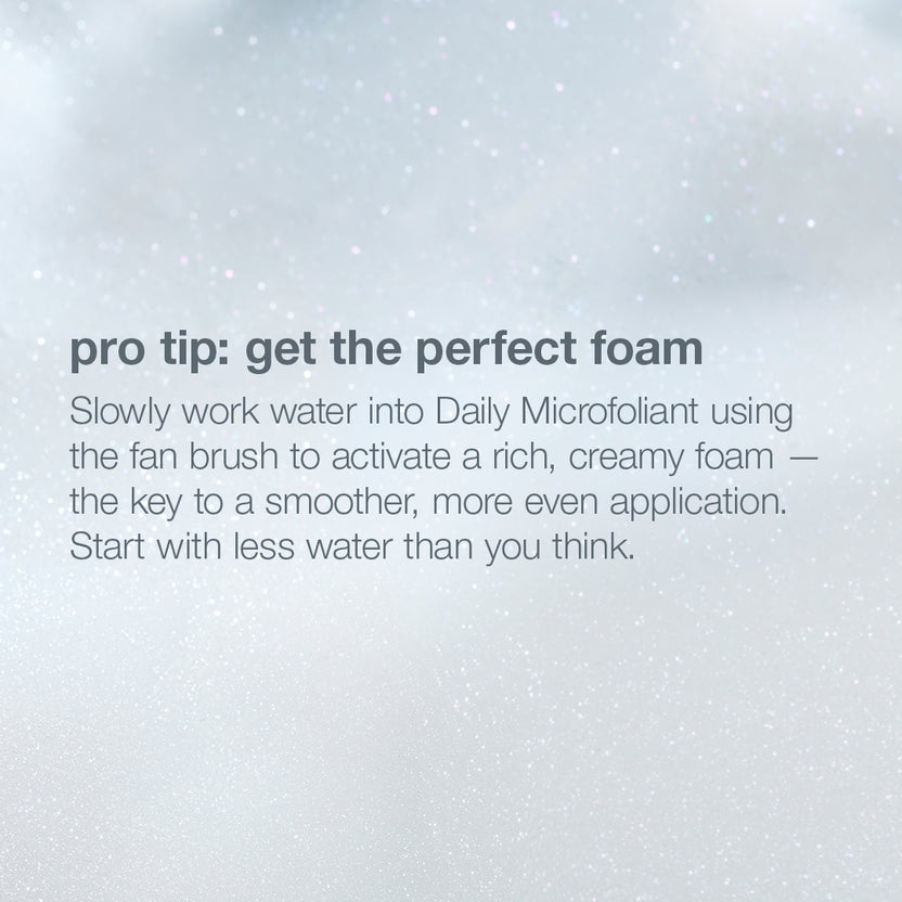 A text-based beauty tip graphic on a soft white and light gray background with faint speckled texture. The text reads: 'pro tip: get the perfect foam' followed by instructions about mixing water into Daily Microfoliant with a fan brush to activate rich, creamy foam.