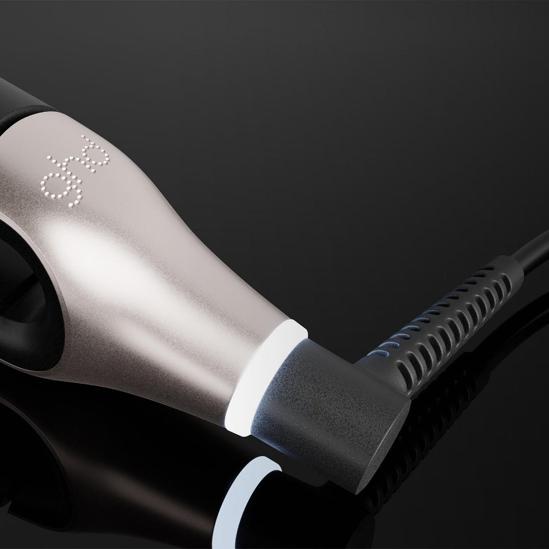 A close-up of a black and silver hair straightener plugged into a black power cord against a dark reflective background.
