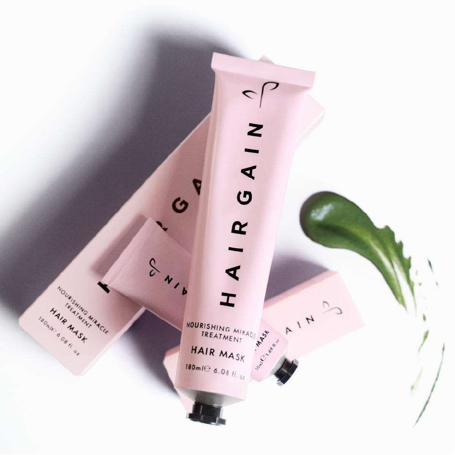 Three pink HAIRGAIN hair mask bottles on a white background with a green leaf.
