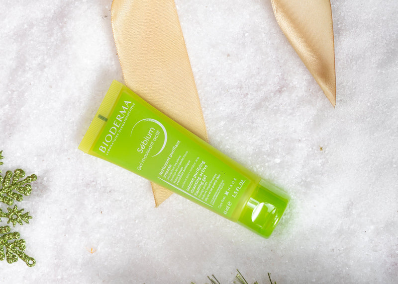 Green skincare product with gold bow on a snowy background