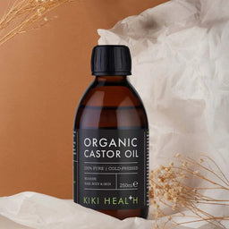Bottle of KIKI Health Organic Castor Oil on a neutral background with dried plants.