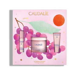Caudalie Fermeté Solution gift set in a pink box decorated with purple grapes, a green leaf, and an orange sun. The set includes a jar, a small bottle, and a tube of skincare products.