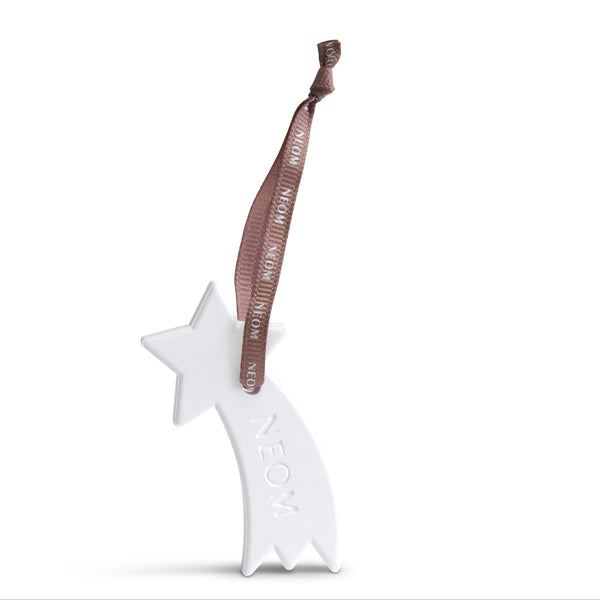A white ceramic shooting star Christmas ornament with the word 'NEON' embossed on its tail, featuring a brown ribbon hanger printed with 'Merry Christmas in Neon'.