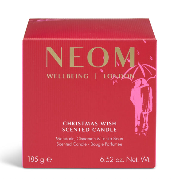 A red square box for a scented candle with gold and white text reading NEOM WELLBEING | LONDON and CHRISTMAS WISH SCENTED CANDLE, plus a pink illustration of a couple under an umbrella on a white background.