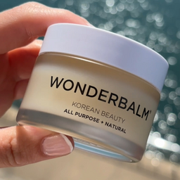 Hand holding a jar of Wonderbalm against a blurred natural background