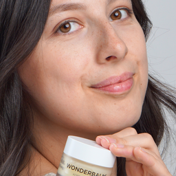 Woman holding a jar of Wonderbalm against a neutral background
