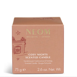 A square cardboard scented candle box by NEOM, labeled 'Cosy Nights Scented Candle,' in a dusty rose color with gold lettering and a small fireplace illustration on the front, photographed on a clean white background.