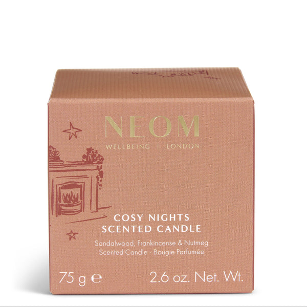 A square cardboard scented candle box by NEOM, labeled 'Cosy Nights Scented Candle,' in a dusty rose color with gold lettering and a small fireplace illustration on the front, photographed on a clean white background.
