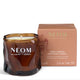 NEOM Cosy Nights scented candle in a dark amber glass jar next to its dusty pink packaging box, on a clean white background.