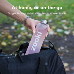 Person holding a pink water bottle labeled 'zooki' with text about single serving sachets for convenience.