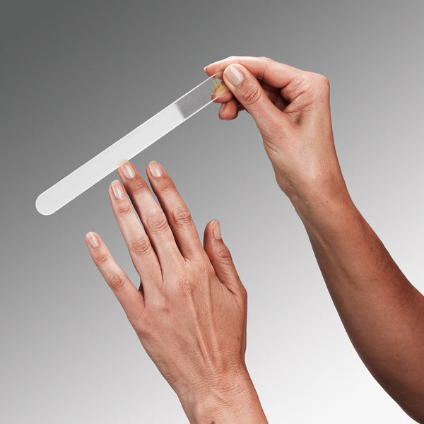 Person using a glass nail file on their hand against a gray background
