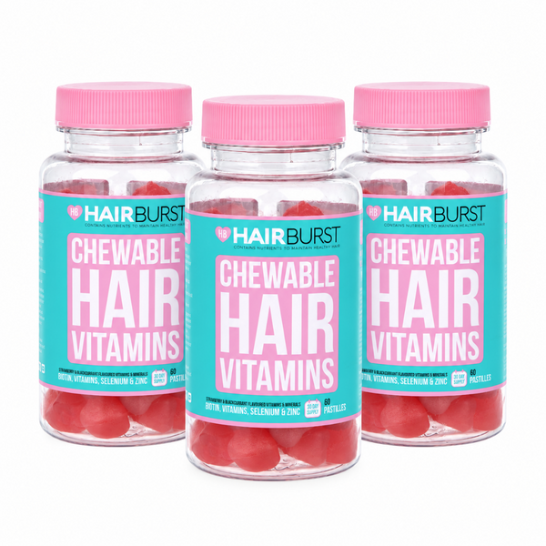 Three clear plastic bottles of Hairburst Chewable Hair Vitamins with bright pink caps and turquoise labels, arranged in a clean studio shot on a white background.