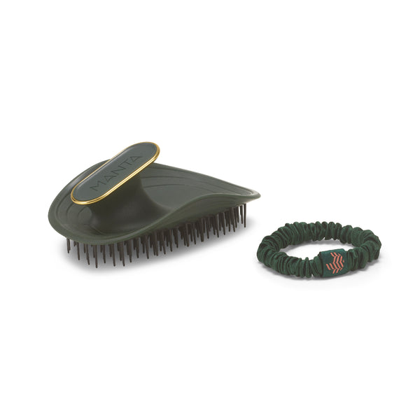 A dark green hairbrush with a gold trim and black bristles next to a matching dark green elastic hair tie with a small red logo, on a white background.