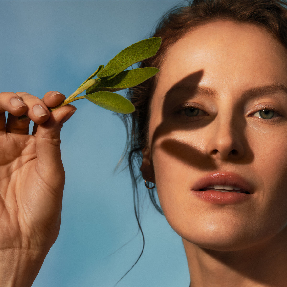 Woman holding a green leaf against a blue sky
