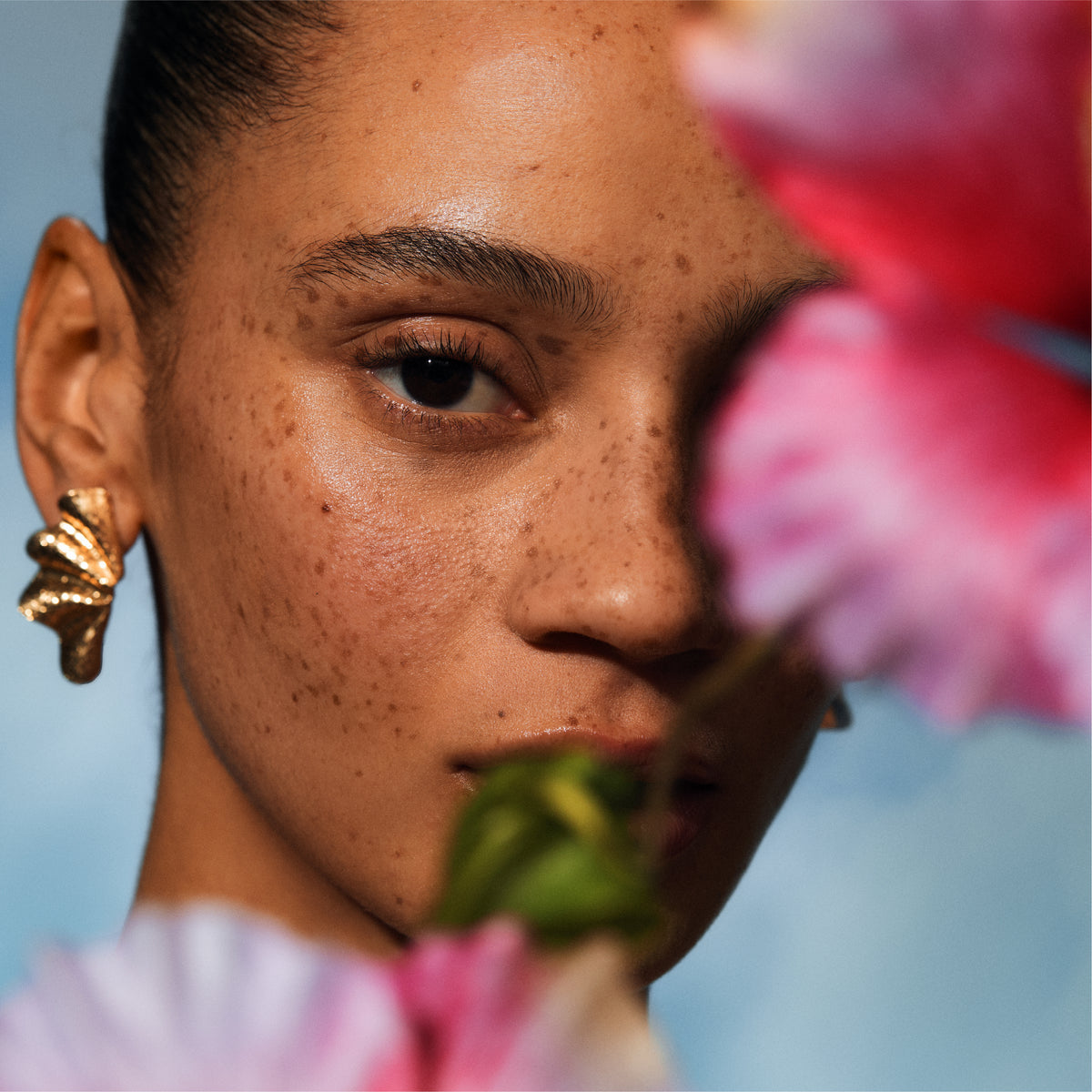 Close-up of a person with freckles holding pink flowers against a blurred background