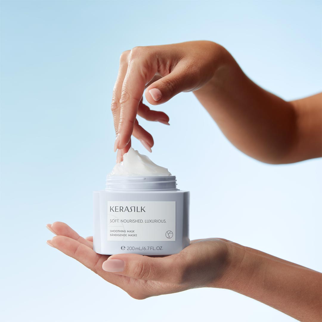 Hand holding a jar of KERASTILK product with a blue background