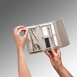 Manicure set in a beige case held by hands against a gray background