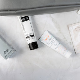 Skincare products on a marble surface with a gray bag.
