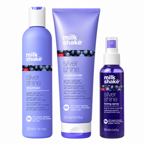 Three Milk Shake haircare products on a white background: a purple shampoo bottle, a matching conditioner tube, and a smaller purple-toning spray bottle.