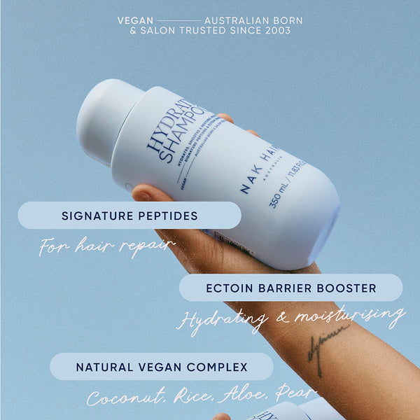 Nak Hydrate shampoo bottle held by a hand with product details on a light blue background