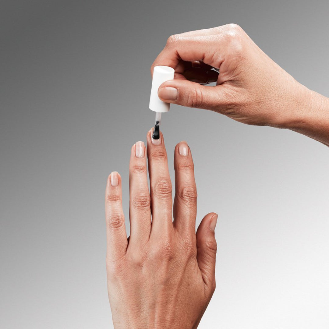 Hand applying nail polish to another hand against a gray background