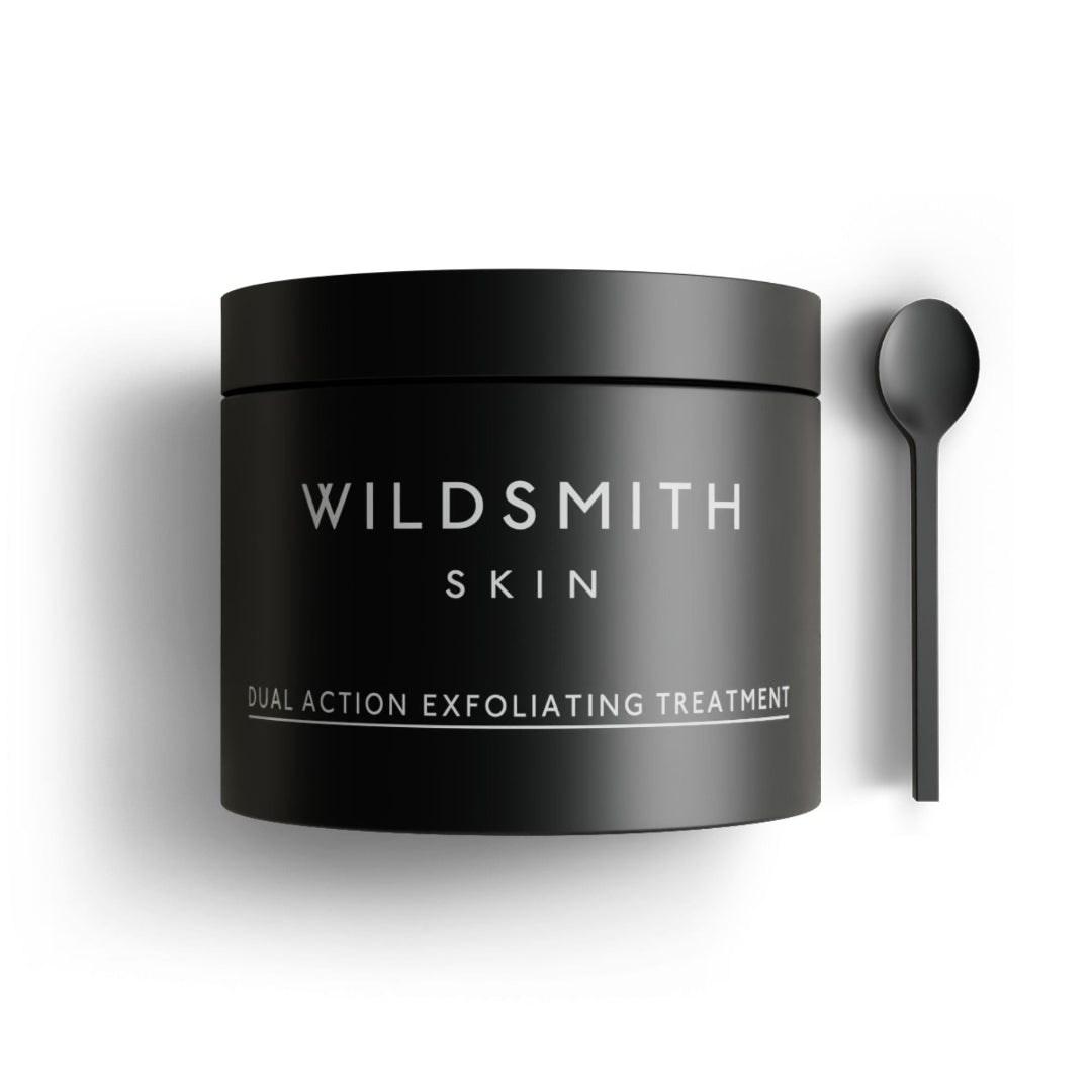 A matte black jar of Wildsmith Skin Dual Action Exfoliating Treatment, shown next to a matching black spoon on a clean white background.