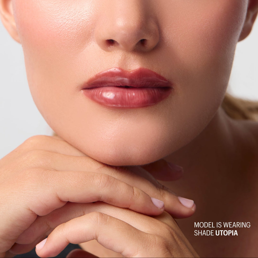 Close-up of a model wearing a glossy, muted rosy-brown lip color, with the text 'MODEL IS WEARING SHADE UTOPIA' in the bottom right corner.