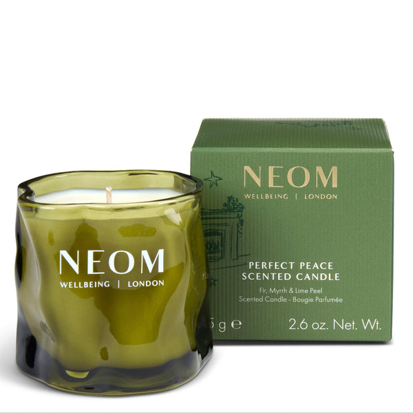 A NEOM Wellbeing London scented candle in a wavy olive-green glass jar, shown next to its matching green box packaging on a clean white background.