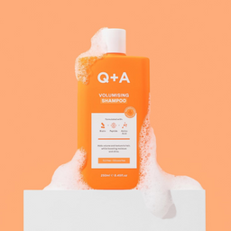 Q+A volumising shampoo bottle with foam on an orange background