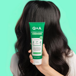 Person holding a Q+A Strengthening Conditioner tube with long dark hair against a green background