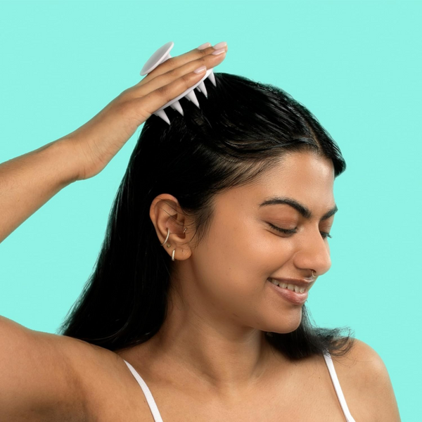 Woman using a hair product on her hair against a teal background
