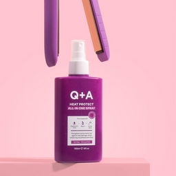 Purple bottle of Q+A Heat Protect All-In-One Spray on a pink background