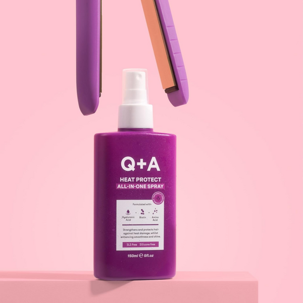 Purple bottle of Q+A Heat Protect All-In-One Spray on a pink background
