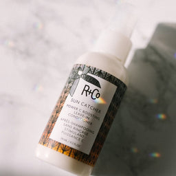 a closeup of a R+Co Sun Catcher Vitamin C Leave In Conditioner bottle