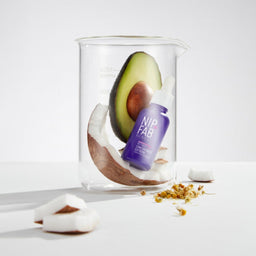 A bottle of the booster in a glass jar with a half of coconut and avocado 