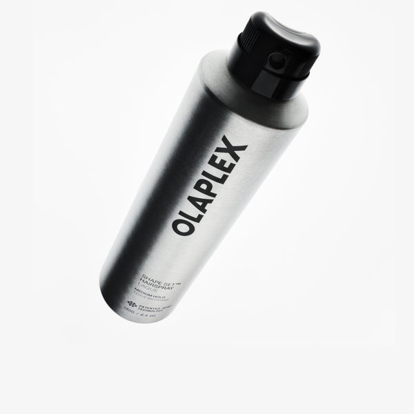 A silver aluminum can of OLAPLEX Shape Set Hair Spray with a black cap, shown floating against a solid white background.
