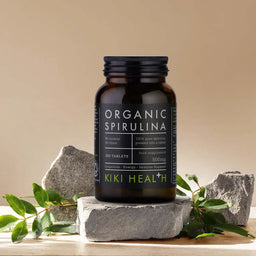 KIKI Health Organic Spirulina supplement bottle on a stone surface with green leaves and rocks in the background.
