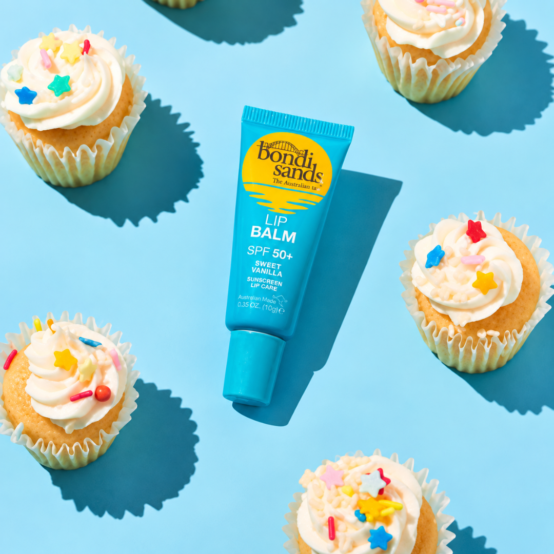 A tube of Bondi Sands Lip Balm SPF 50+ in Sweet Vanilla, styled on a bright blue background with cupcakes around it.