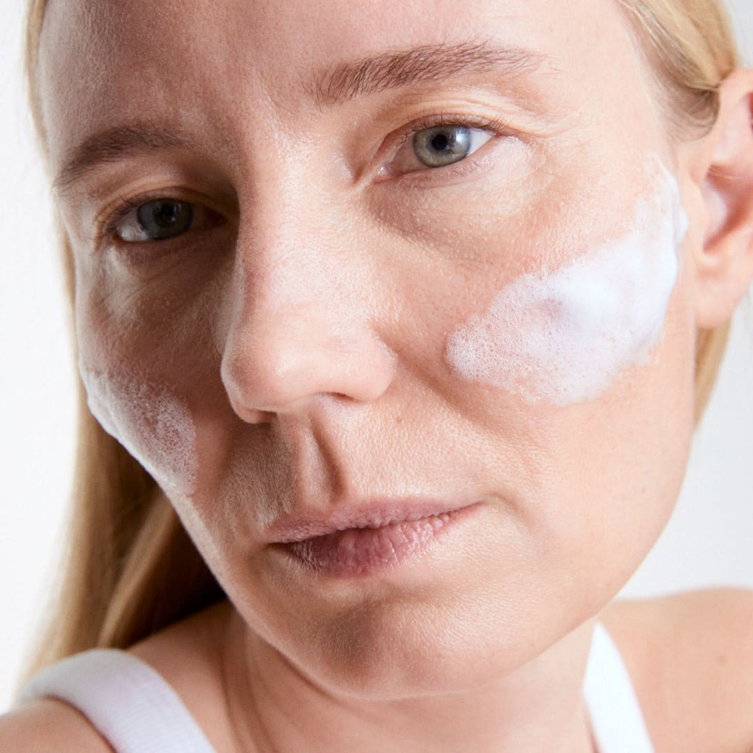 Woman applying a white cream to her face with a neutral background