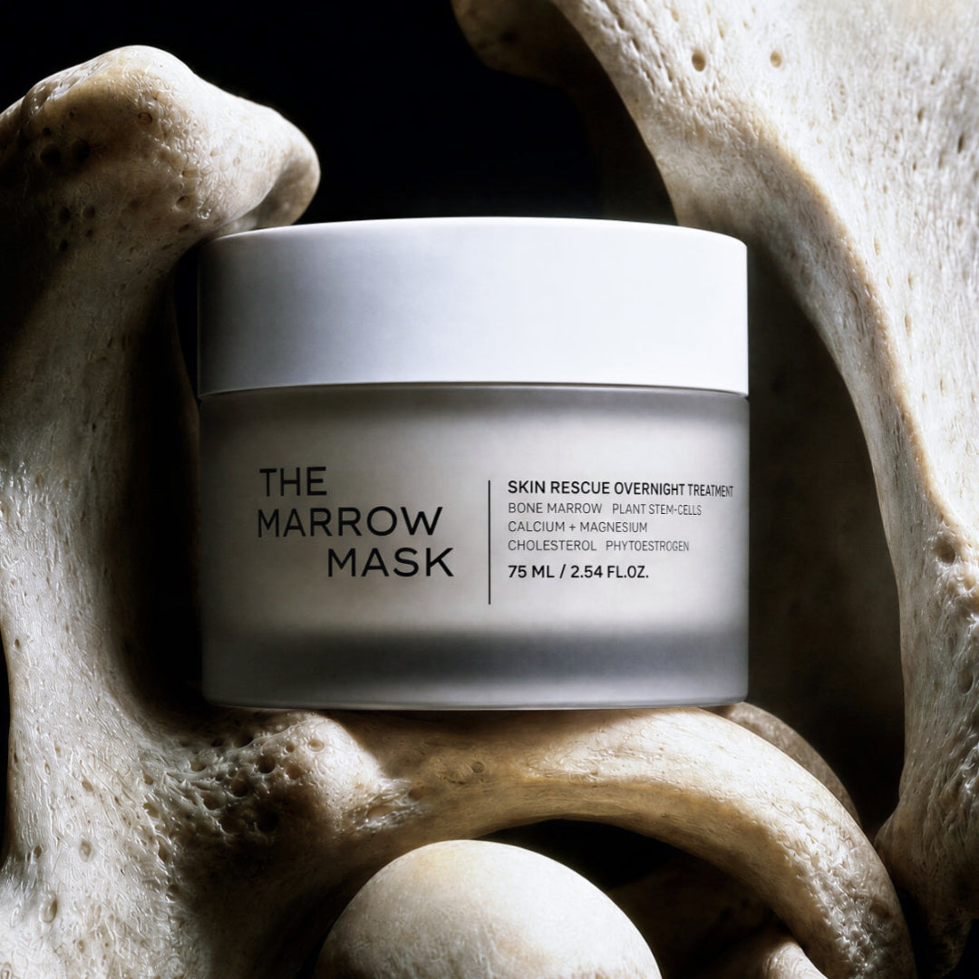 A frosted glass jar of 'The Marrow Mask' skincare product, displayed on a bed of large beige bones against a dark background.